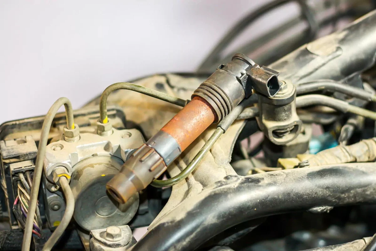 An old rusty ignition coil sitting on a dusty engine.