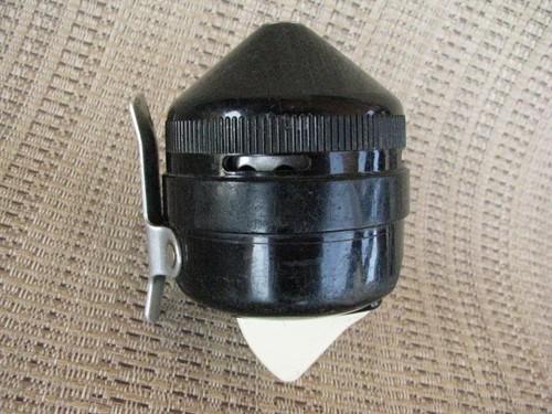 Black vintage Zebco 202 spin casting reel with silver handle, made in USA, shown against a textured beige background.