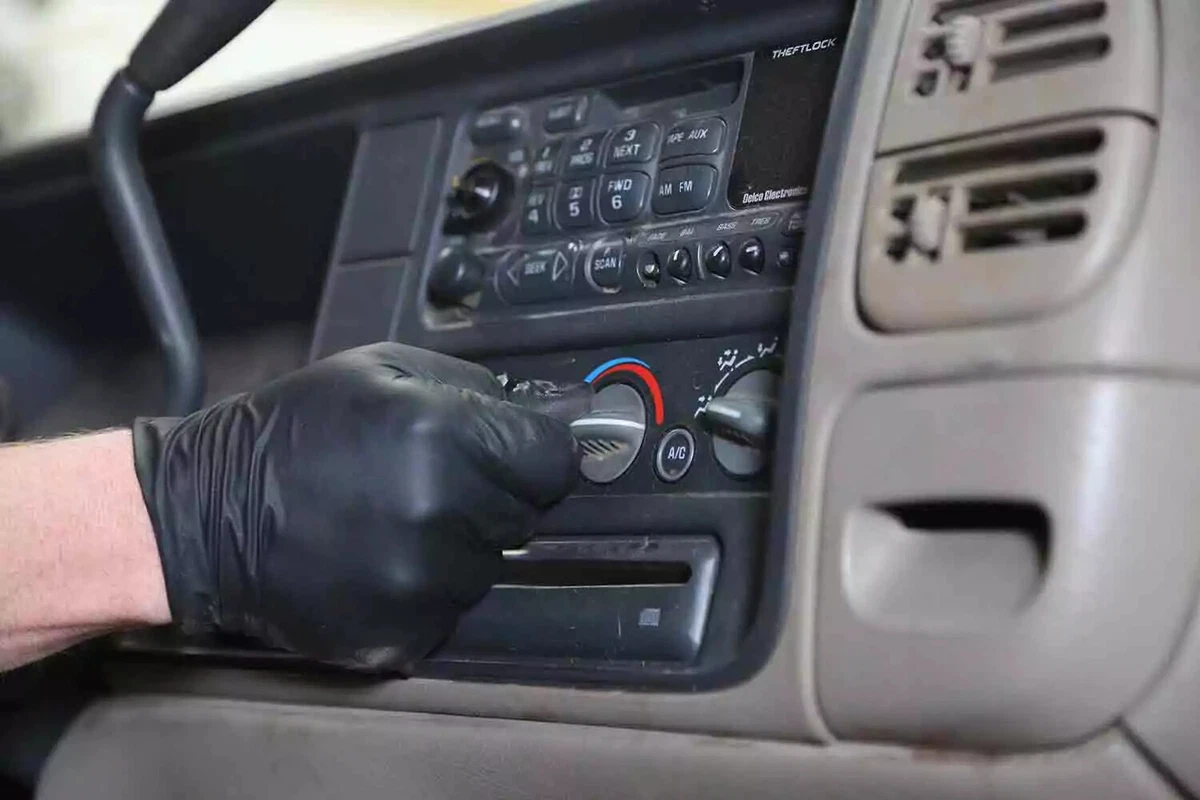A mechanic wearing a black glove turns on the vehicle's heater.