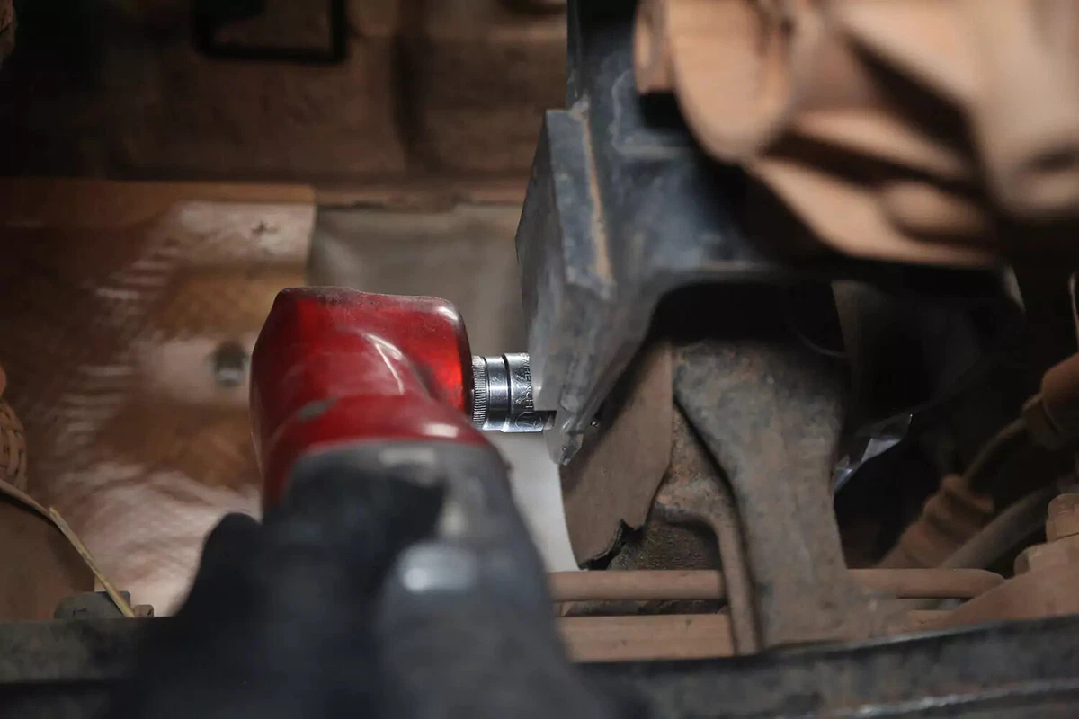 A mechanic uses an impact wrench to loosen a crossbolt.