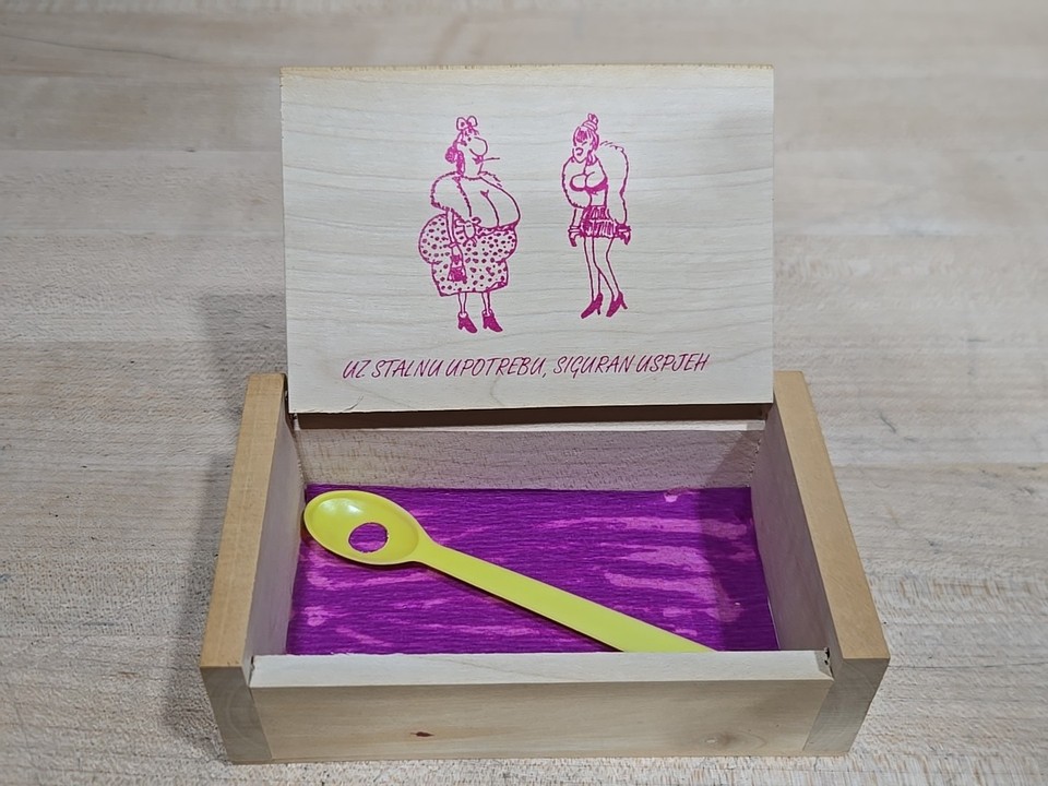 A carved wooden Yugoslavian 'diet spoon' gag — a tiny trinket box with a peephole joke inside, pure Cold War–era absurdist humor.