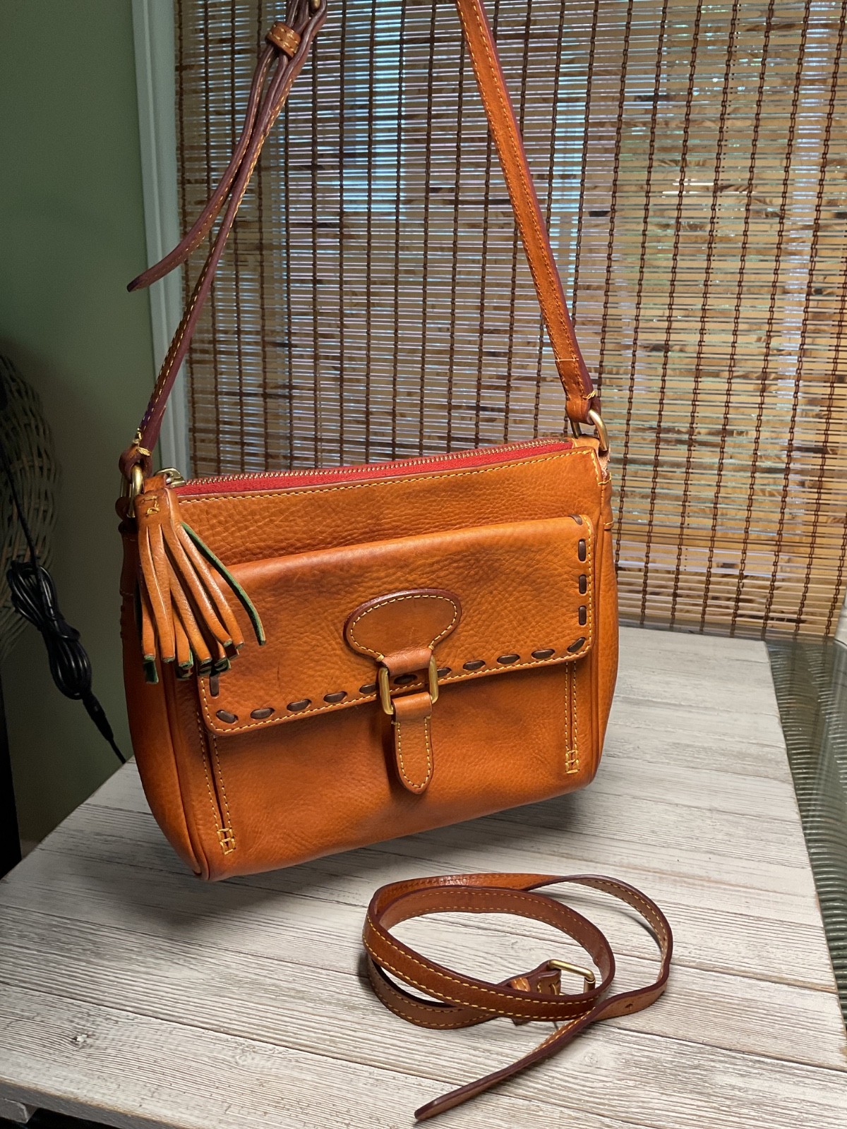 Tan brown leather crossbody bag with a buckled front pocket and detachable strap.