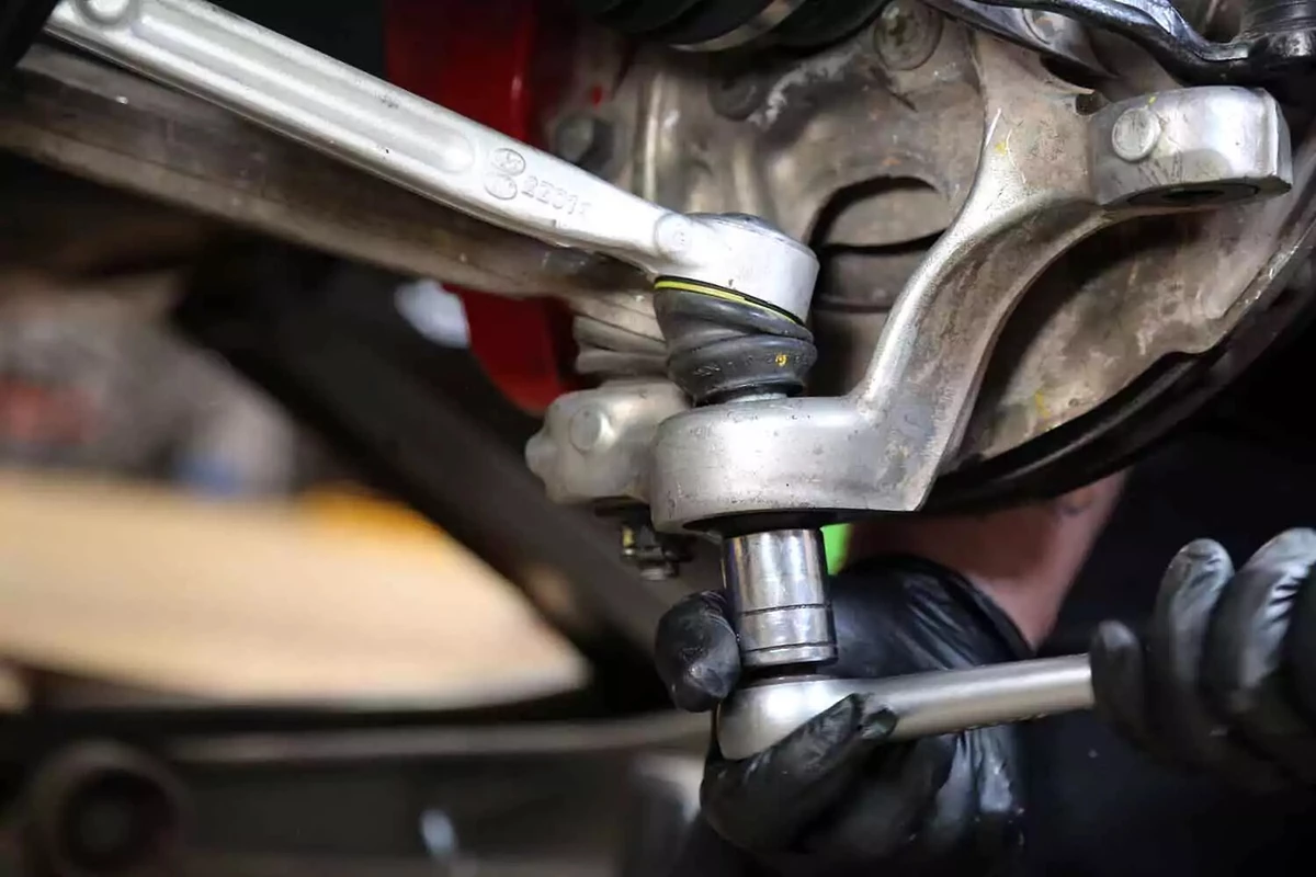 A mechanic refastens a ball joint and tie rod end with a socket wrench.
