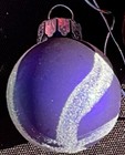 Round purple Christmas ball with diagonal white stripes and silver cap, made in a dark patterned background.