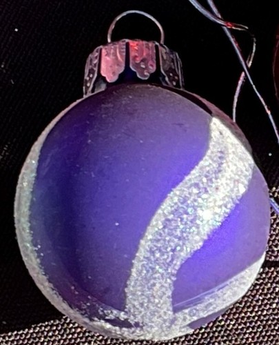 Round purple Christmas ball with diagonal white stripes and silver cap, made in a dark patterned background.