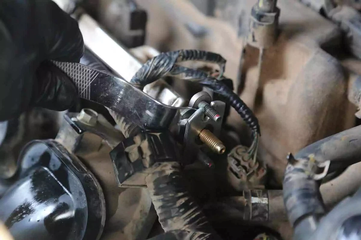 A mechanic wearing a black glove uses a pry tool to remove the fuel-line adapter.