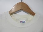 White short-sleeve Sz L Vtg men’s T-shirt with blue “Hanes” label and wooden hanger against plain background.