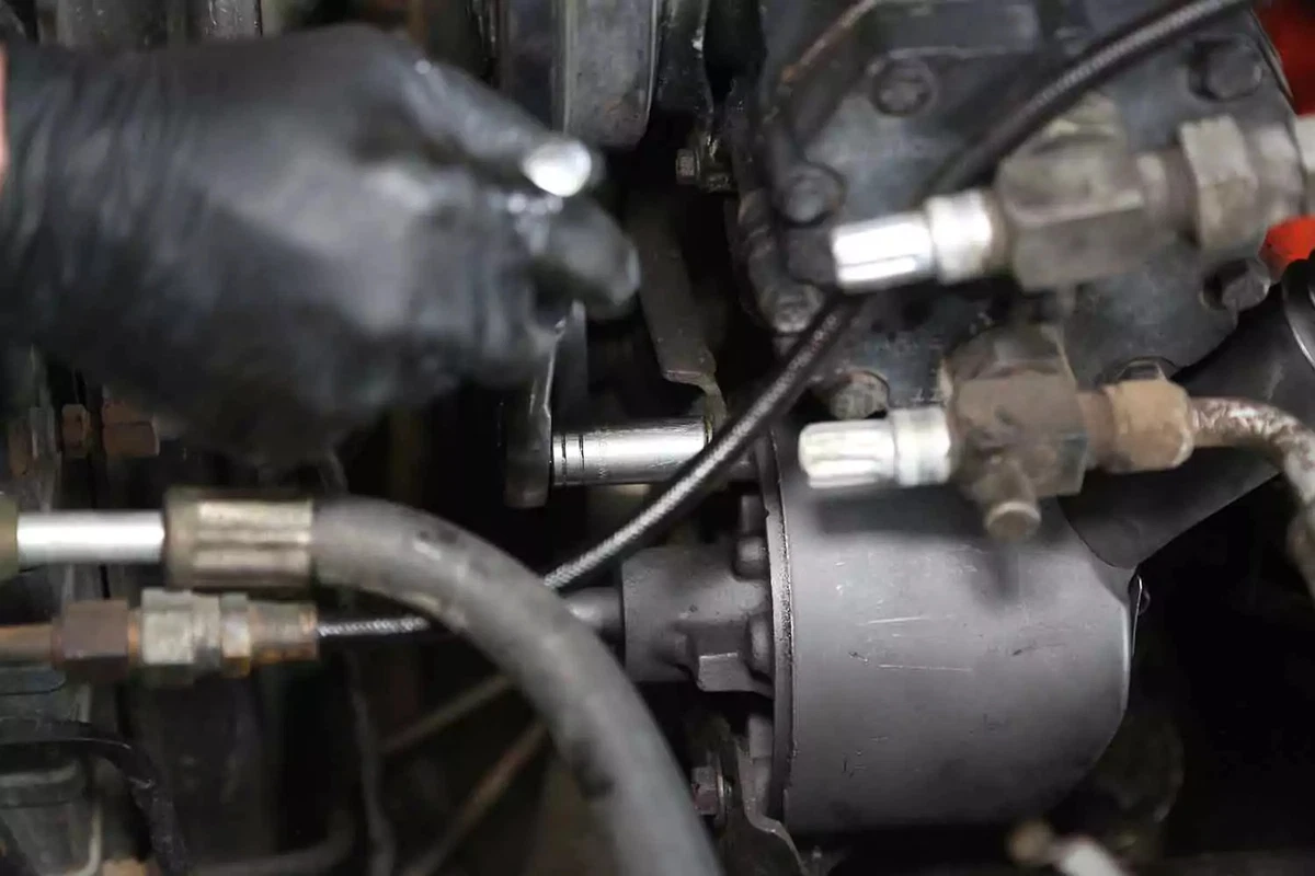 A mechanic tightens a bolt on the new power steering pump with a socket wrench.