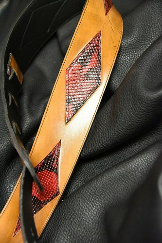 Black leather guitar strap with tan inlay featuring red and black diamond pattern and two black strap anchors.