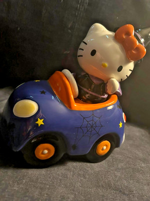 HELLO KITTY in witch costume, driving orange & purple car celebrating HALLOWEEN