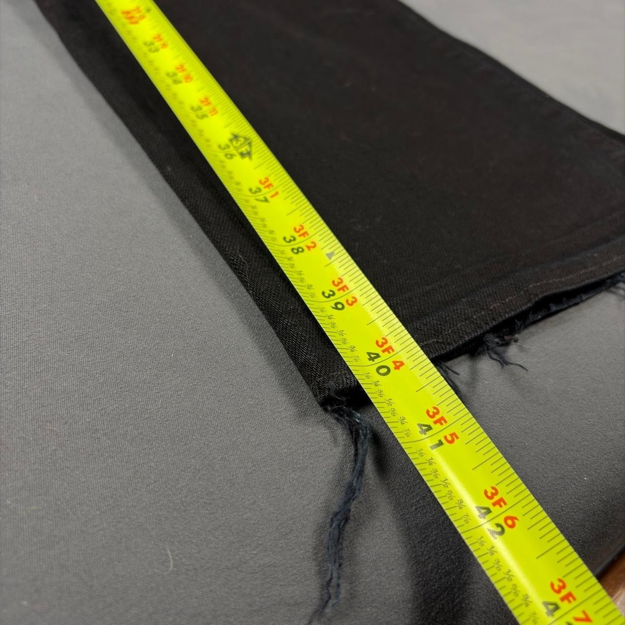 Black denim bootcut jeans with frayed hems, yellow measuring tape along the waistband, showing size 3F 4A.