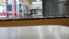 Light wood electric guitar with gold hardware and three pickups, shown on a gray measuring tape across the fretboard.