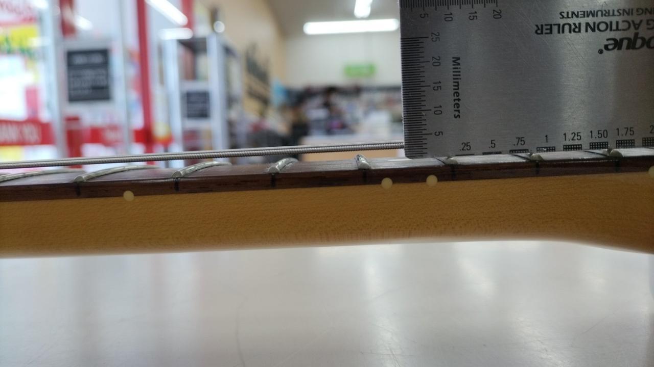 Light wood electric guitar with gold hardware and three pickups, shown on a gray measuring tape across the fretboard.