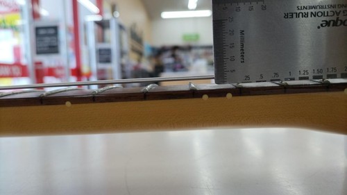 Light wood electric guitar with gold hardware and three pickups, shown on a gray measuring tape across the fretboard.