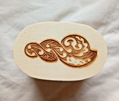 Kleine ovale aufklappbare Holzkiste mit Maori (?) Symbol auf Deckel plus ''om'' Stein