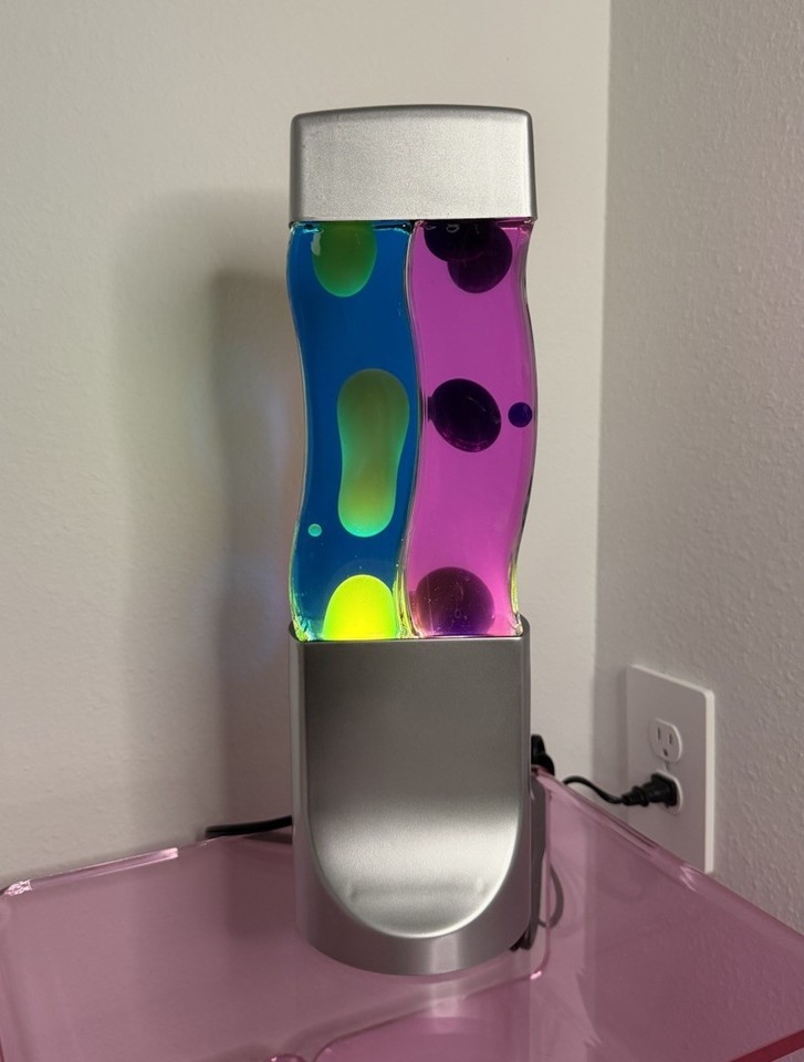 A dual-motion wavy lava lamp in blue, pink, and yellow — the groovy silhouette and tri-color palette make it a living sculpture, not just a light.