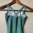 Green and silver holographic Destira gymnastics leotard with thin straps and scalloped lace trim on wooden hanger.