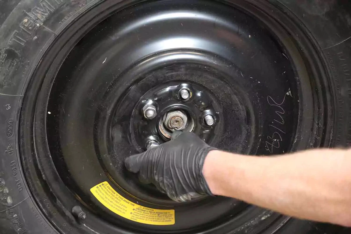 A mechanic wearing black gloves threads lug nuts onto a vehicles emergency spare tire.