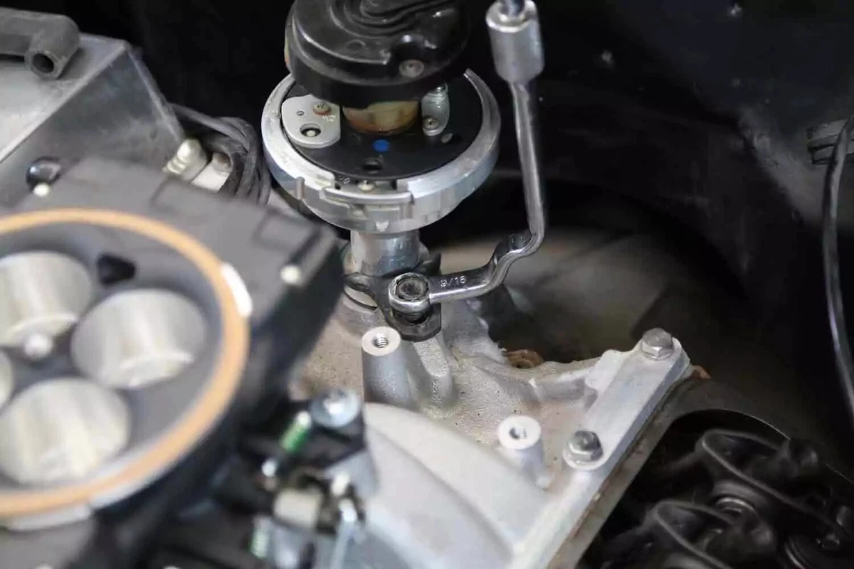 A mechanic fastens a new distributor to a V-8 engine with a specialized distributor clamp wrench.