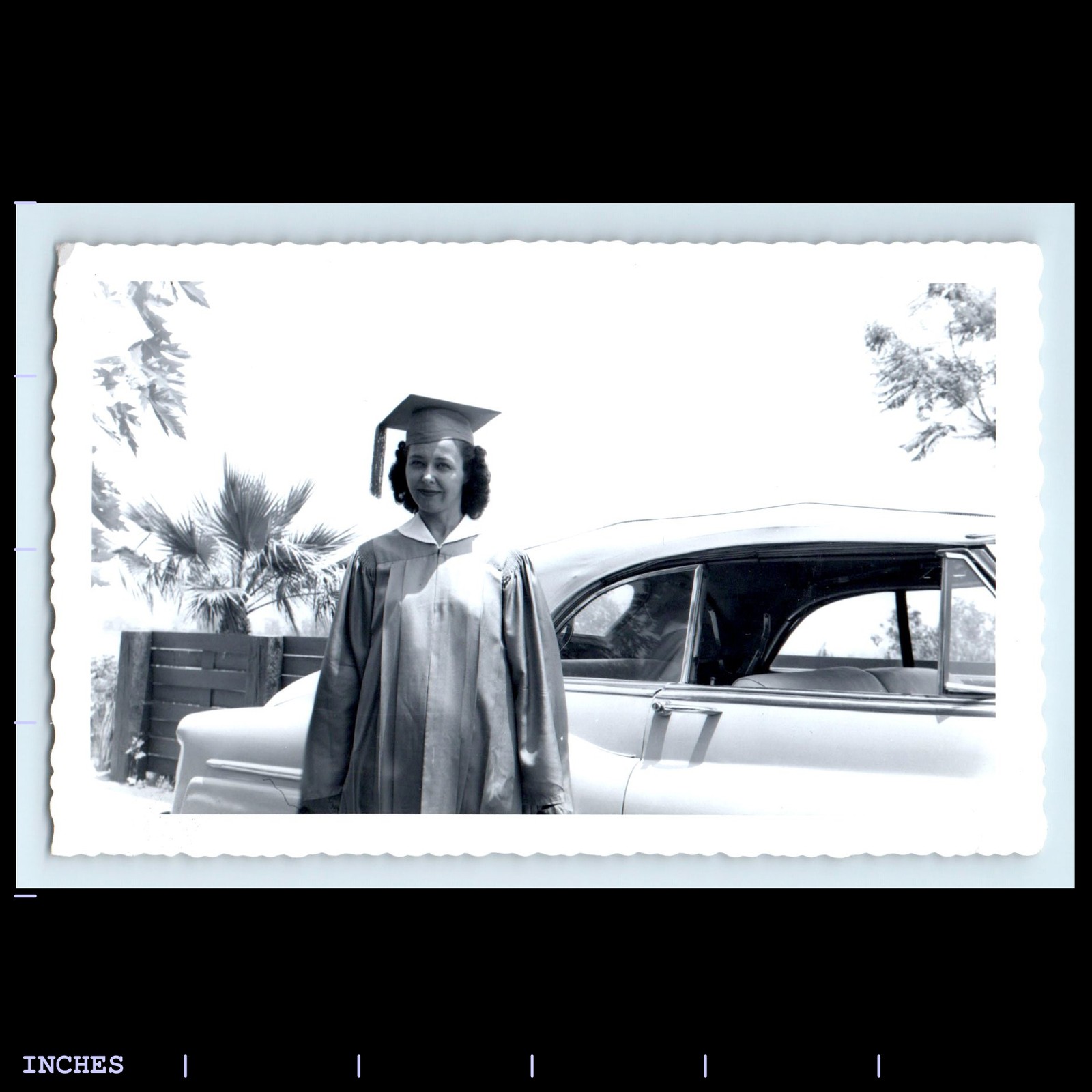 Vintage photo of woman in graduation cap and gown with classic car