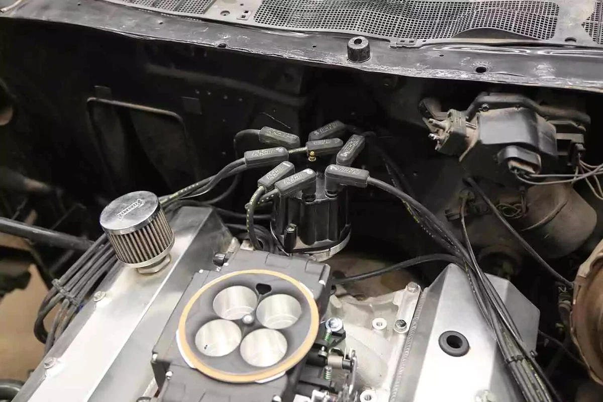 A distributor with a black cap sits between a high-performance V-8 engine and the firewall.