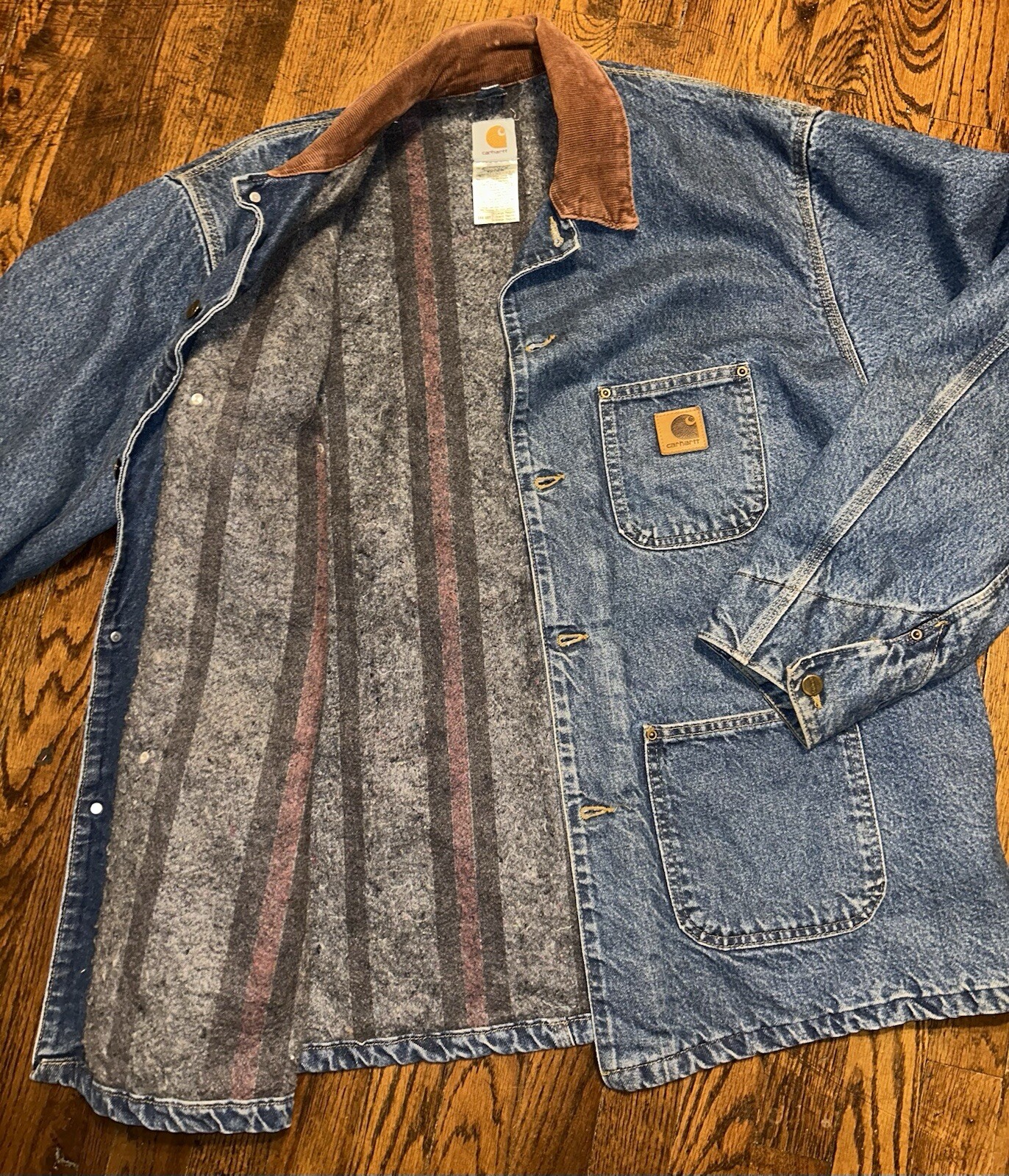 Blue denim Carhartt C59DST chore coat with brown collar, front pocket, and visible Carhartt logo patch on chest.