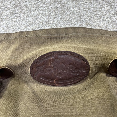 Brown canvas crossbody bag with dark brown leather strap, featuring embossed logo patch on front.