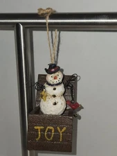 snowman in a "jack-in-the-box" style container that says "JOY" on the front.