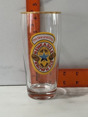 Newcastle Brown Ale 16 schooner glass featuring a gold rim.