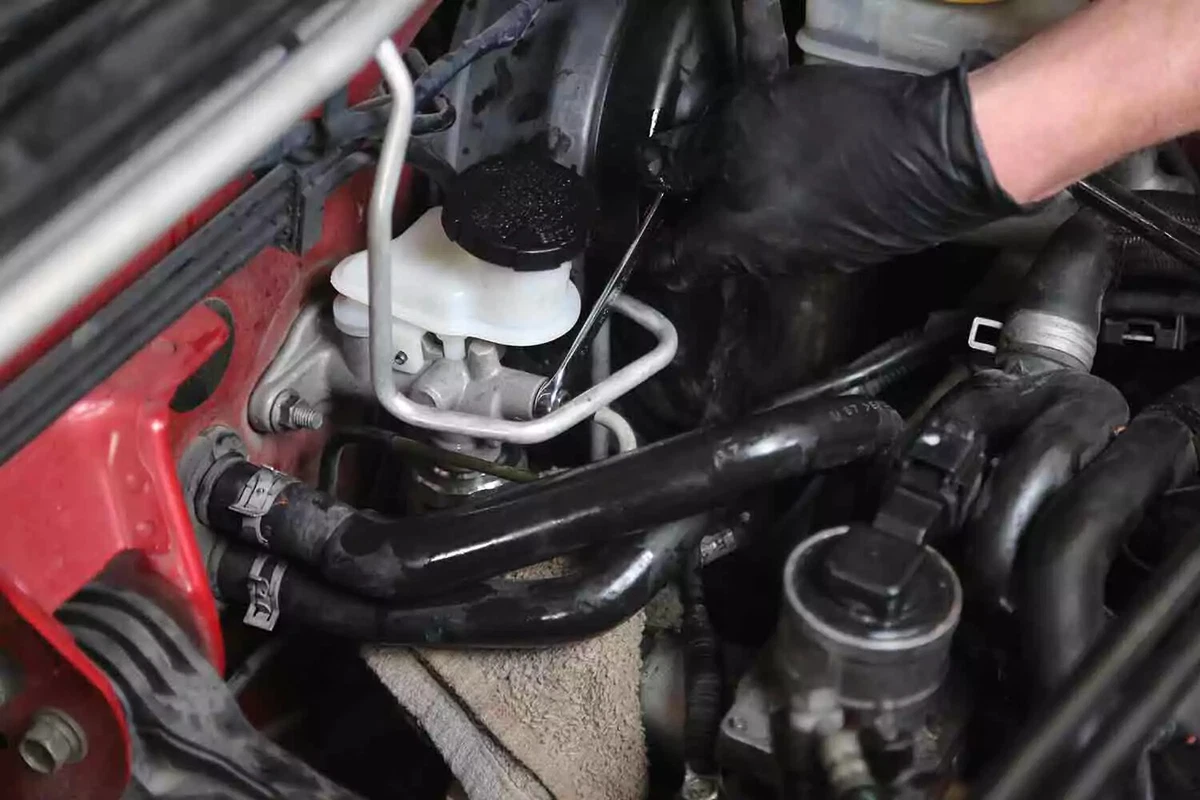 A mechanic wearing black nitrile gloves tightens a fitting on a brand new clutch master cylinder with a wrench.