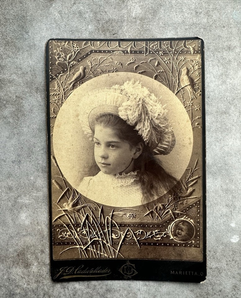 A genuinely eerie, visually arresting Victorian cabinet photo pairing an elaborately hatted woman with a disturbingly expressionless crying baby — pure antique oddity gold.