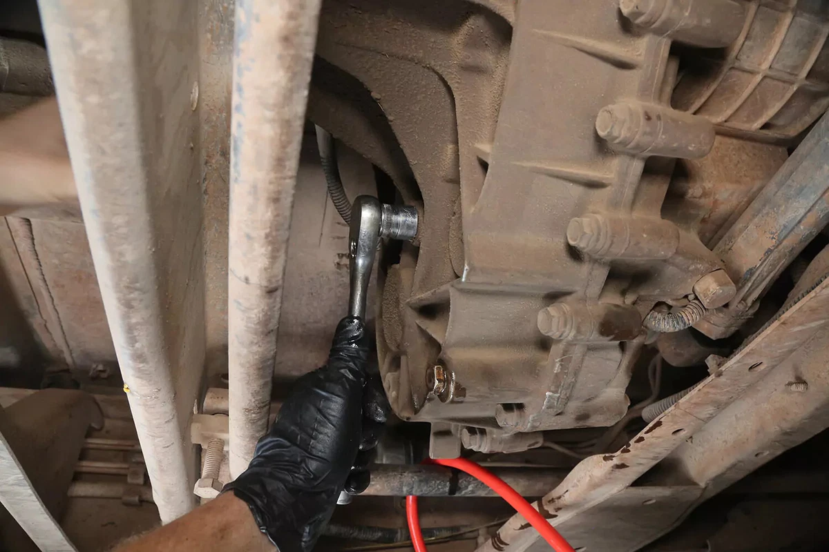 A mechanic uses a socket to remove the fill plug from the transfer case.