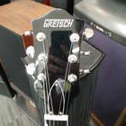 Black GRETSCH G6119 TENNESSEE ROSE full-body electric guitar with silver hardware and three pickups, standing in front of speakers.