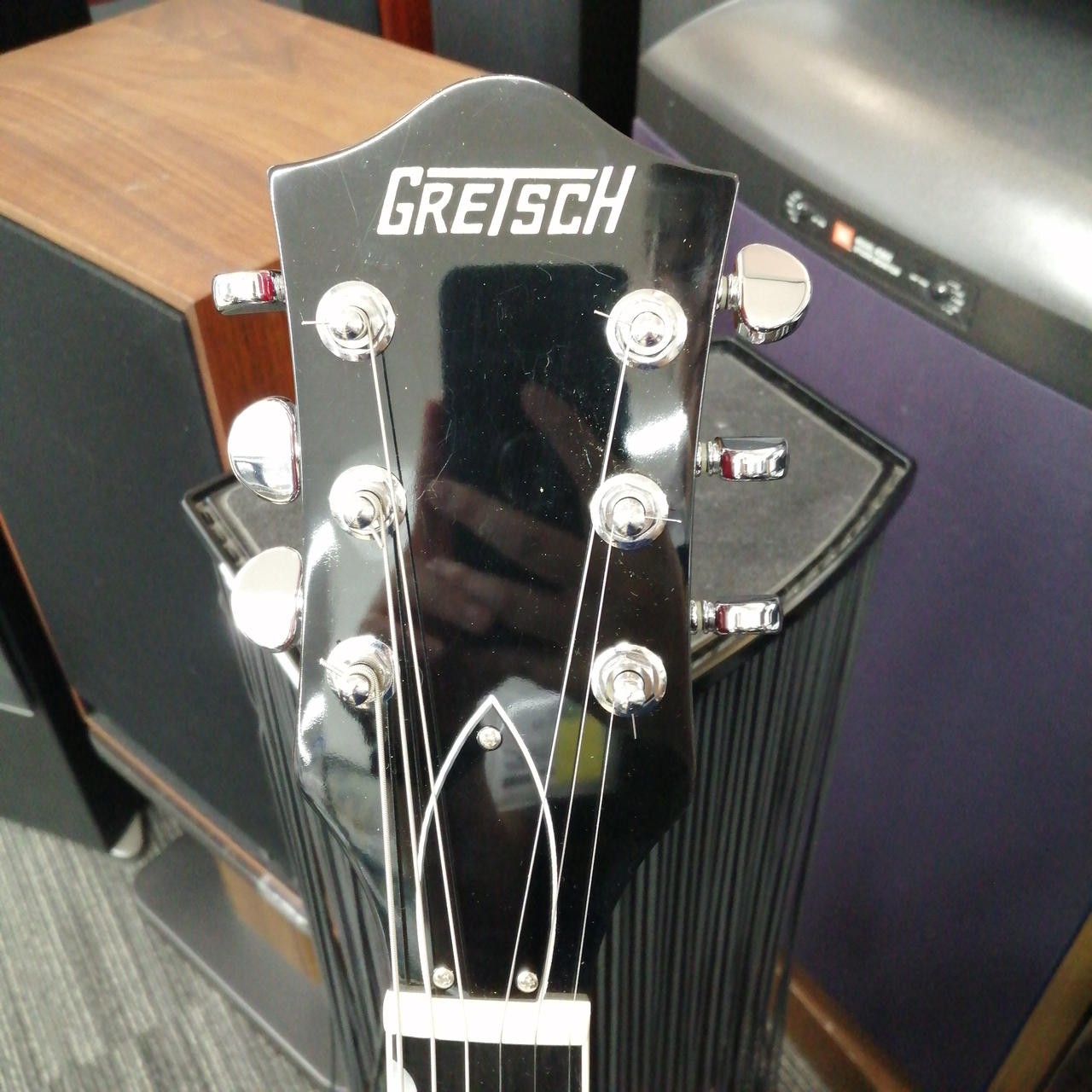 Black GRETSCH G6119 TENNESSEE ROSE full-body electric guitar with silver hardware and three pickups, standing in front of speakers.