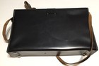 Black leather shoulder bag with visible seams, brown adjustable strap, and “Made in U.S.A.” text on top.