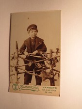 Boy with hat behind fence with toy bat / CDV Hermann Tietz Hamburg