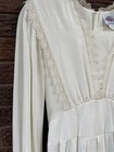 White vintage midi prairie dress with long sleeves, lace trim neckline, and fitted bodice on wooden surface.