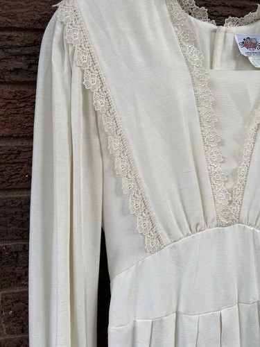 White vintage midi prairie dress with long sleeves, lace trim neckline, and fitted bodice on wooden surface.