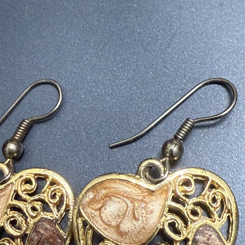 Gold-tone dangle drop earrings with filigree swirl design and round hammered gold accents on a dark background.