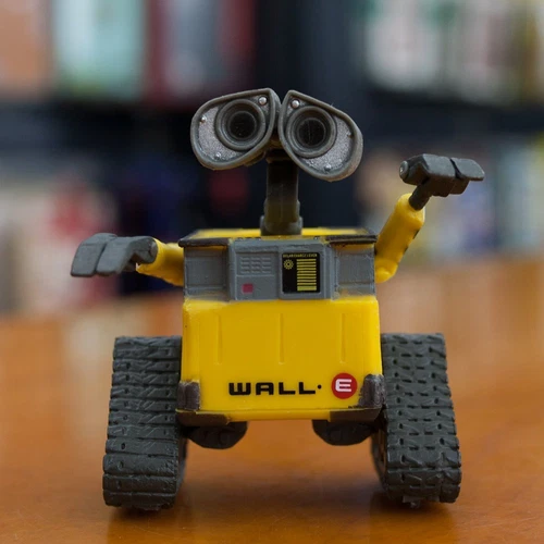 Yellow WALL-E robot toy with gray panels, large binocular eyes, and treaded wheels on a wooden surface.