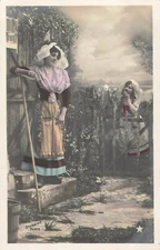 CP LITTLE GIRL WITH FLOWER POT BEHIND BARRIER WOMAN LEANING WITH RAKE 31740