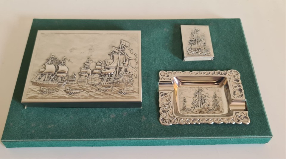 A silver-plated naval desk set with cigarette box, ashtray, and matchbox holder — a genuinely cinematic relic of old-world office ritual.