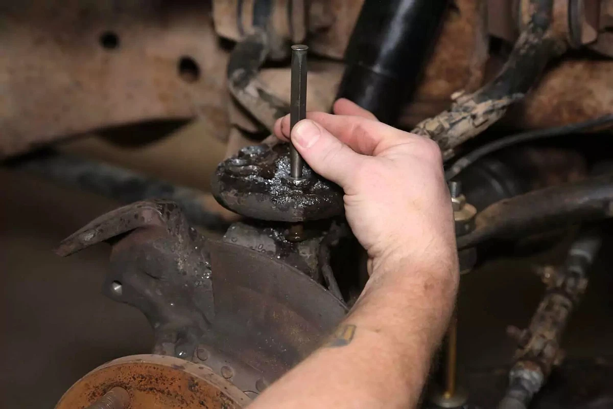 A mechanic uses a pinch and hammer to knock out a rivet.
