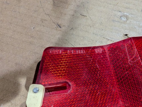 Red vintage 1970s 1980s Micro-Flex bike rim reflector with gold reflection points and mounting hole on brown surface.