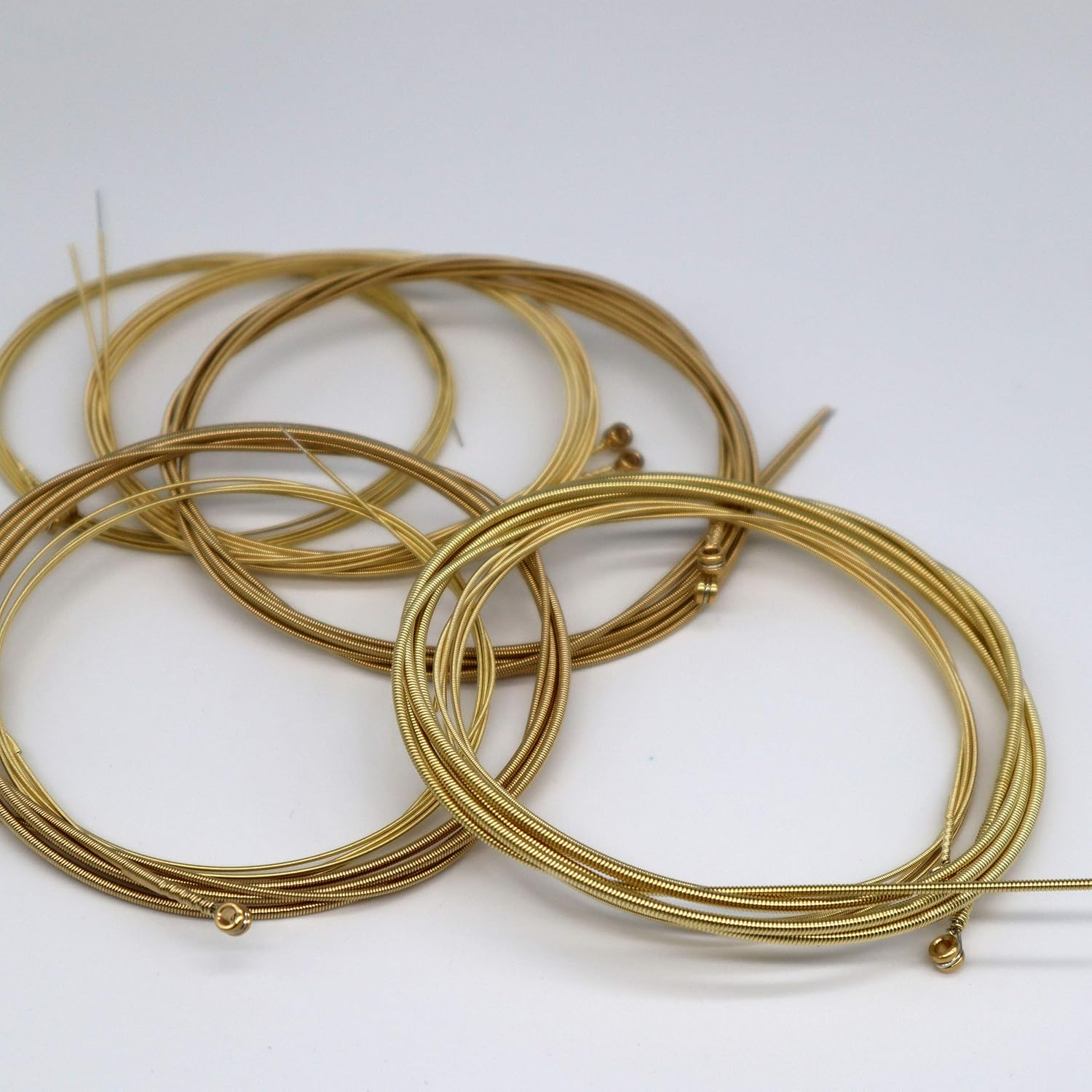 Gold-wound guitar strings with black ball ends on white background, arranged in clear plastic packaging.