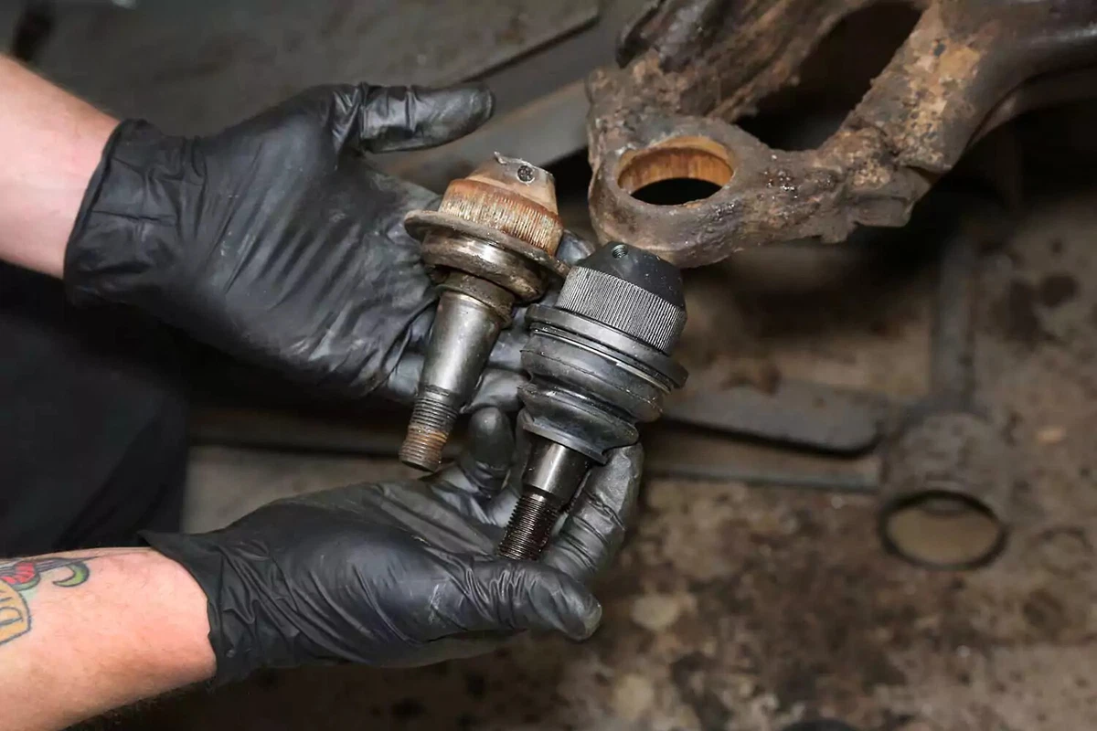 A mechanic compares the old and new ball joints.