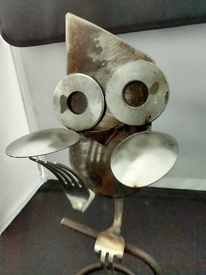 Búho esculpido sentado en soporte hecho de cucharas, tenedores, arandelas y metal Foto 2 de 4