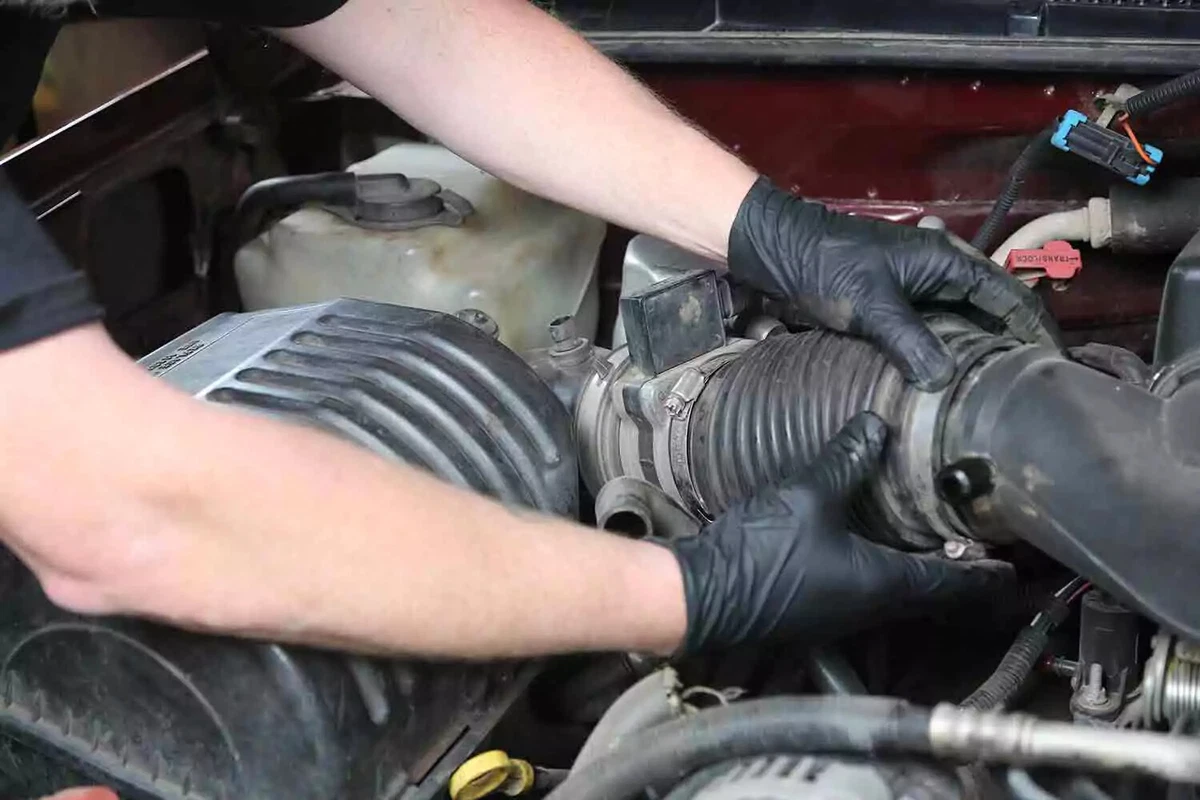 A mechanic wearing black gloves reinstalls components removed earlier.