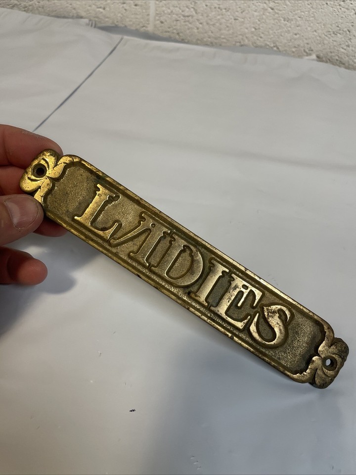 A solid brass vintage 'Ladies Room' door plaque with real patina and heft — the kind of thing boutique hotels pay a designer to source.