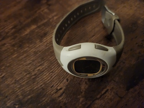 Gray vintage Polar F6 heart rate monitor watch with white dial, black buttons, and adjustable strap on wooden surface.